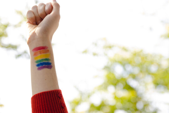 Image of hand of caucasian non-binary trans woman with painted rainbow flag