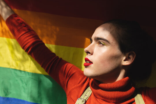 Image of profile of caucasian non-binary trans woman holding rainbow flag