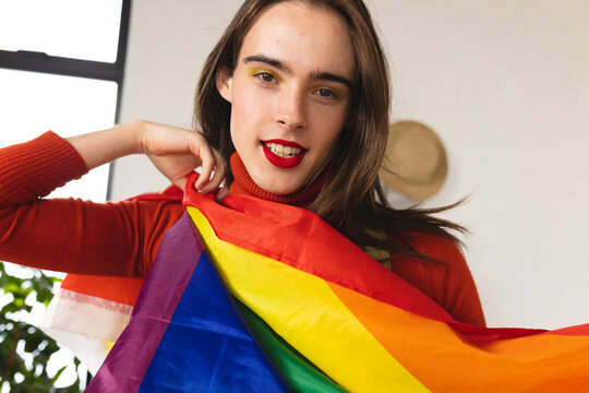 Image of happy caucasian non-binary trans woman holding rainbow fabric