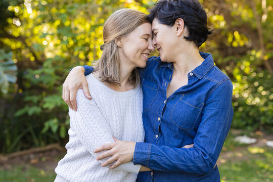 Smiling caucasian mid adult lesbian couple with eyes closed romancing and cuddling against plants