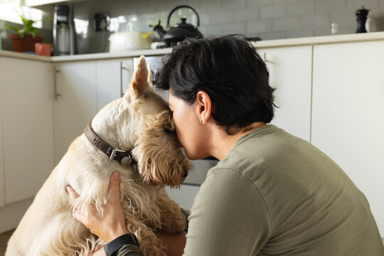 Side view of caucasian mid adult lesbian woman kissing scottish terrier while sitting in kitchen