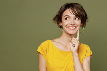 Young fun smiling minded dreamful happy woman she 20s wear yellow t-shirt look aside on workspace area mock up isolated on plain olive green khaki background studio portrait. People lifestyle concept.