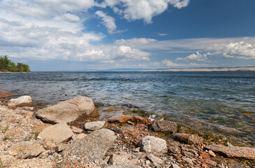 Siberian Baikal Lake. A beautiful summer landscape with a rocky shore of the Small Sea and a green forest in the distance on a sunny day. Natural background. Travel and recreation on the lake