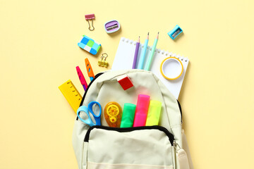 Backpack with colorful school supplies on yellow table, top view. Back to school concept. Flat lay,...