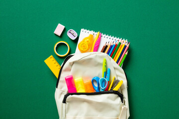 Backpack with school stationery on green background. Back to school concept. Flat lay, top view.