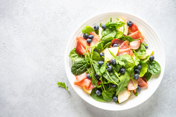 Healthy salad with spinach, jamon, pear and blueberry. Top view on white background.