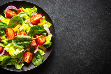 Fresh salad in black craft plate. Vegan meal. Top view with copy space.