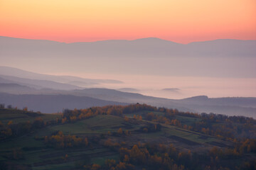 misty autumn morning. gorgeous countryside scenery in mountains at dawn. forested hills and glowing fog in the distance valley