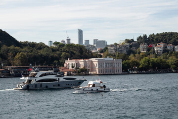 View of a yacht and fishing boat passing on Bosphorus and Baltalimani neighborhood on European side of Istanbul. It is a sunny summer day. Beautiful travel scene.