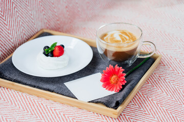 Cup of coffee, Pavlova dessert cake, gerbera flower and blank postcard with copy space on the tray with gray napkin. Breakfast for loved one. Romantic surprise. Take a break, relax. Selective focus.