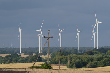 ENERGETICS - Medium-voltage line fastened on a concrete pole and wind farm turbine on background