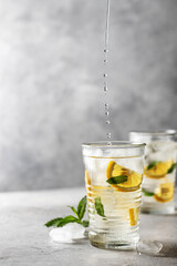 Two glasses of summer iced refreshing drink lemonade with lemon, mint and ice cubes on gray background with text space on the left