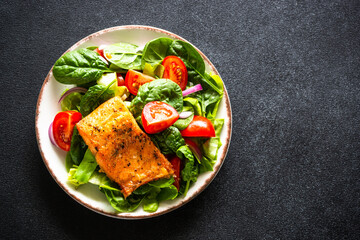 Green salad with salmon fillet in white plate. Healthy lunch, diet nutrition. Top view on black.