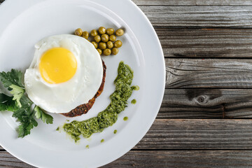 Scrambled eggs with meat on a plate, garnished with green peas and pesto sauce.