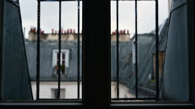 Conceptual image of a window on a rainy day: in the foreground the glass with rain drops, in the background blurred the view of the roofs with vintage attics.