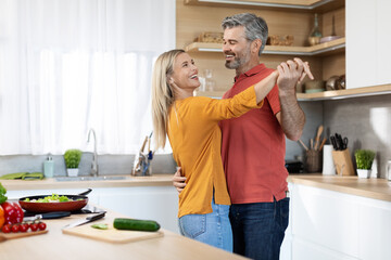 Romantic middle aged couple dancing while cooking together