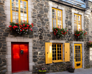 Fototapeta na wymiar Beautifully preserved patrimonial stone house with red door and yellow shutters in the old town Sous-le-Fort street, Quebec City, Quebec, Canada