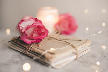 Romantic paper folded letters laced with rose flowers on table close up over glow lights. Snail mail and old memories.