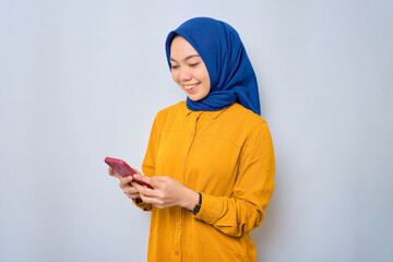 Smiling young Asian Muslim woman dressed in orange using mobile phone, typing SMS messages isolated over white background