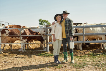 Obraz premium Happy farmer couple hugging near paddock with cows