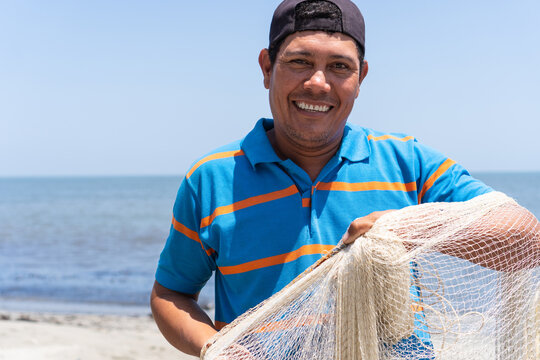 Smiling Portrait Of Latino Fisherman With Fishing Net In HandLatino Fisherman Checking His Cell Phone On The Beach