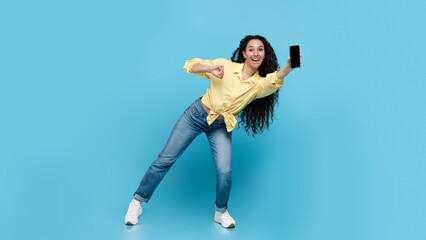 Obraz premium Cheerful Middle Eastern Woman Showing Phone Posing On Blue Background