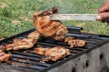 Man overturning meat on barbeque with meat gripper, food preparation