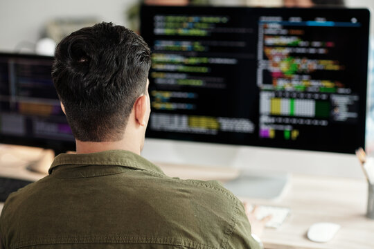 Software developer looking at programming code on computer screen, view from back