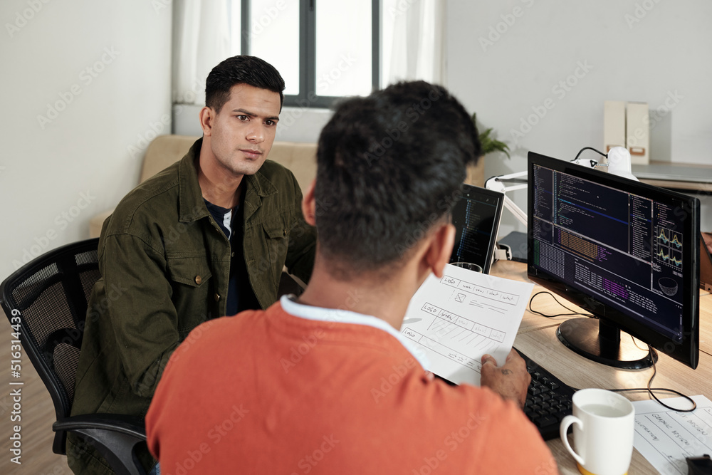 Wall mural serious software developer listening to ideas of front end developer at meeting