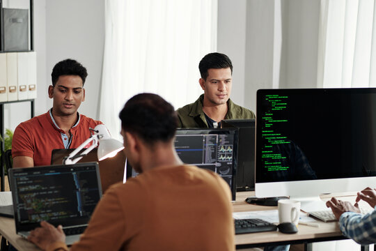 Group of young Indian devops engineers working in modern office, coding and maintaining updates
