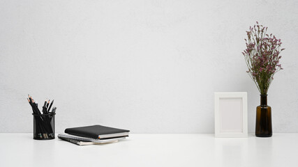 Minimal workplace with picture frame, pencil holder and books on white table