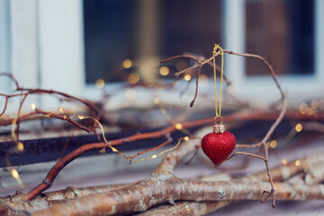 Christbaumschmuck rotes Herz mit Zweigen und Weihnachtsbeleuchtung im Hintergrund