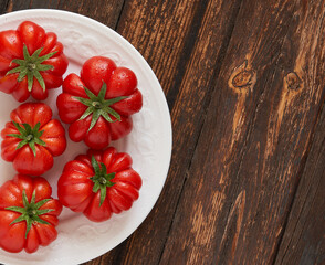Fresh red tomatoes raf, on white plate on wooden background. Food concept