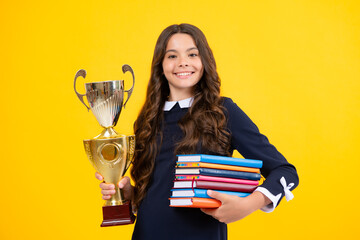 Schoolgirl in school uniform celebrating victory with trophy. Teen holding winning prize on yellow background. School kid win gold trophy.
