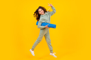 Child girl dressed in sports uniform. Run and jump. Child in a posh stylish sports suit in a hoodie with a hood hold yoga mat. Advertising sportswear tracksuit. Healthy kids lifestyle, sport.