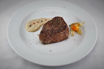 Pepper steak on a white plate with sauce and physalis