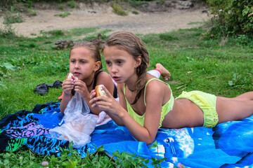 Two little girls on a green lawn eat a bun