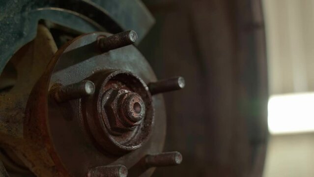 An auto mechanic cleans a spacer on a car hub with a metal brush, dressed on a drill, before replacing the brake disc of a car wheel of a raised car at a repair station. 4k