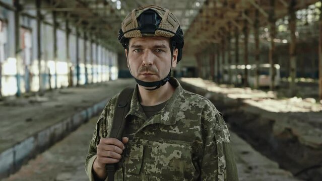 Portrait of confident man from military forces in safety helmet looking at camera while standing at destroyed steel plant. Bravery and fearlessness concept.