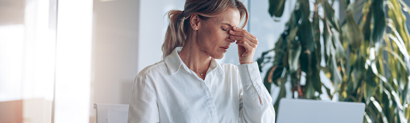 Tired lady boss with headache working on laptop at workplace in modern office. Business concept.