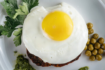 Scrambled eggs with meat on a plate, garnished with green peas and pesto sauce.