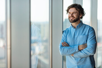 Portrait of confident mature businessman standing near window in modern company office, copy space