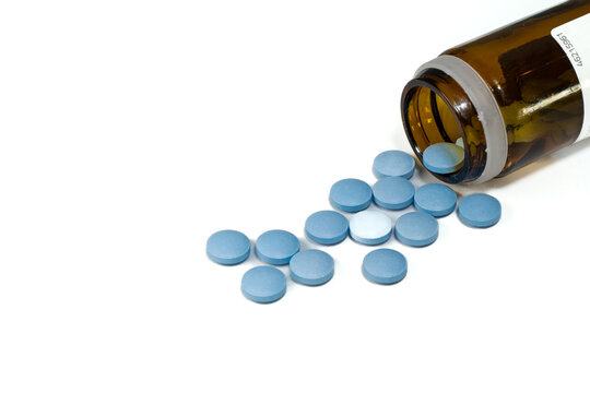 glass bottle with scattered blue pills on white background