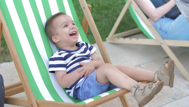 The boy lies on a sunbed and smiles when he is tickled on a bright sunny day in the park at sunset. Family lifestyle. Happy childhood. The boy smiles while having fun in the fresh air
