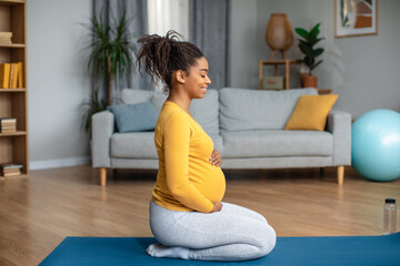 Satisfied peaceful calm young pregnant african american woman sits on mat, practicing yoga and meditation