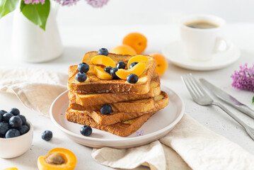 Traditional french toasts with cinnamon, blueberries and apricots. Healthy breakfast recipe. Toasts and a cup of coffee on a table. Bakery, restaurant menu. Good morning concept