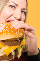 A hungry woman is biting a big tasty burger . Binge eating