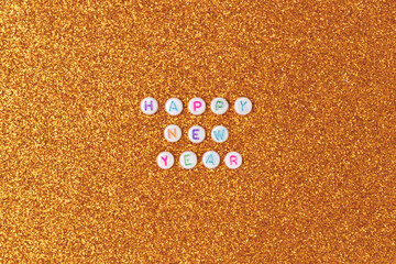 Happy New Year. Quote made of white round beads with colorful letters on a gold glittering background.