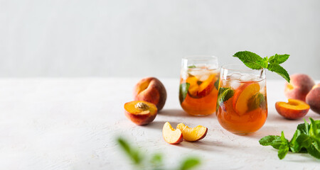 Summer cold peach fizz cocktail or iced tea with mint. Two glasses with peach lemonade on a white...