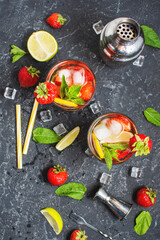 Summer refreshing mojito cocktail with strawberry, mint and lime with shaker for whipping drinks on a dark stone table